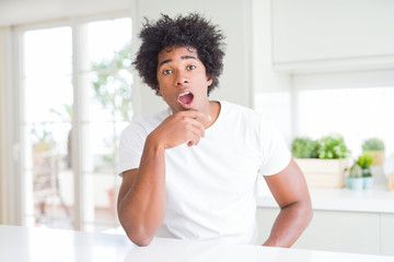 Fototapeta na wymiar Young african american man wearing casual white t-shirt sitting at home Looking fascinated with disbelief, surprise and amazed expression with hands on chin