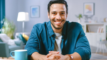 Portrait of Handsome Man Sitting at Desk in His Living Room and Charmingly Smiling. Medium Shot.