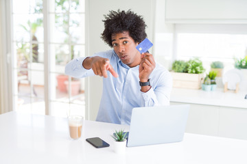 African American man using laptop and shopping online with credit card pointing with finger to the camera and to you, hand sign, positive and confident gesture from the front