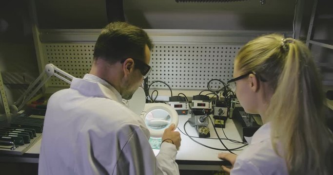Electric engineer teaching young apprentice soldering microchips in workshop