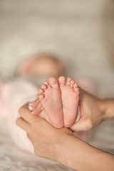 Mother holding her baby's feet on bed, closeup