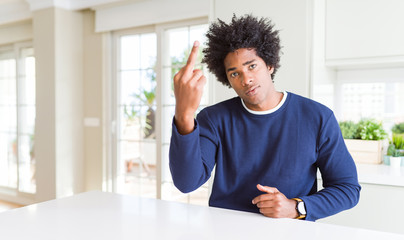 Young african american man wearing casual sweater sitting at home Showing middle finger, impolite and rude fuck off expression