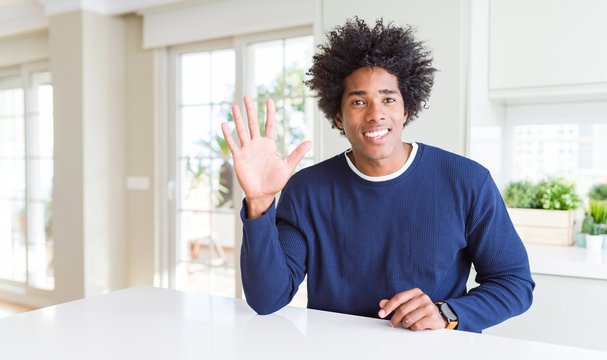 Young african american man wearing casual sweater sitting at home showing and pointing up with fingers number five while smiling confident and happy.