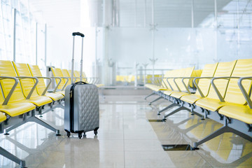 Beautiful gray suitcase for hand luggage in airport terminal with unfocused background of yellow seats, empty waiting area. Vacation trip concept