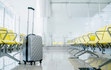 Beautiful gray suitcase for hand luggage in airport terminal or departure lounge with yellow seats with unfocused background, empty waiting area. Vacation trip concept