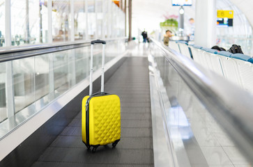 Fototapeta na wymiar Beautiful yellow suitcase stands or left on the moving walkway in the airport. Traveler trip summer vacation concept 