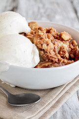 Fresh hot homemade apple crisp or crumble with crunchy streusel topping topped with vanilla bean ice cream. Selective focus with blurred background. 