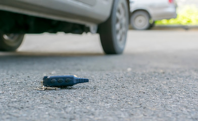 The lost keychain, car alarm remote, lies on the asphalted sidewalk of the road, near an entrance of a house with the parked cars