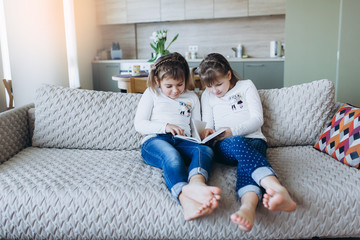 Two cheerful children reading a book together in living room. Childhood, leisure, homework concept