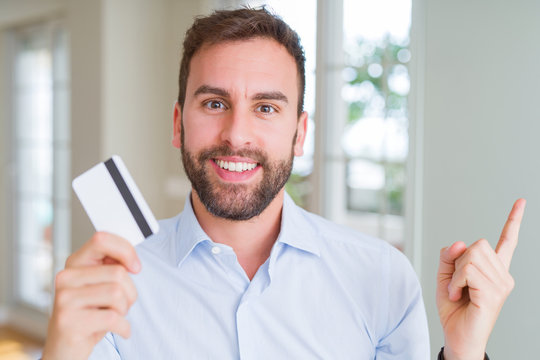 Handsome business man holding credit card very happy pointing with hand and finger to the side