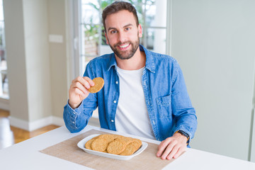 Handsome man eating healthy whole grain biscuit with a happy face standing and smiling with a confident smile showing teeth