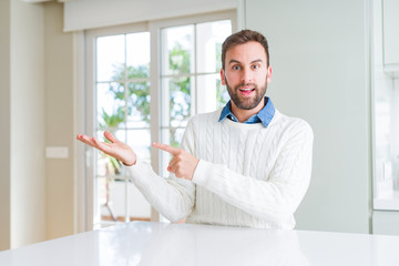 Fototapeta premium Handsome man wearing casual sweater amazed and smiling to the camera while presenting with hand and pointing with finger.