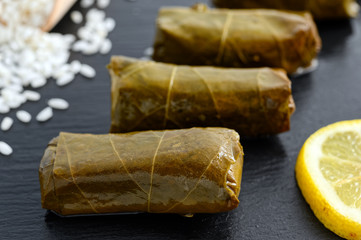 Delicious stuffed grape leaves (the traditional dolma of the mediterranean cuisine) on black dish with lemon slices and raw rice