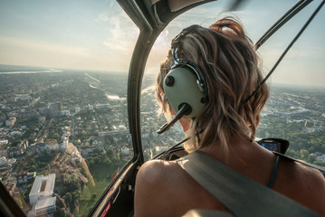Portrait of beautiful blonde women enjoying helicopter flight. She is amazed by cityscape.