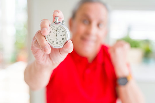 Handsome senior man holding stopwach showing countdown screaming proud and celebrating victory and success very excited, cheering emotion