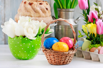 Wicker basket with Easter eggs on the table. Floral decorations in the background.