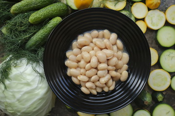 Boiled beans in a black plate on a background of fresh vegetables