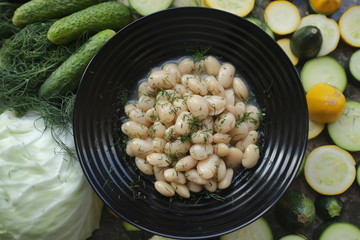Boiled beans in a black plate on a background of fresh vegetables