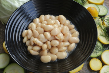 Boiled beans in a black plate on a background of fresh vegetables