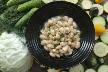 Boiled beans in a black plate on a background of fresh vegetables