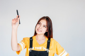 Young smiling girl student worker with dark long hair in yellow t-shirt with graphic pen in hand, isolated on grey background