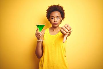 Young african american woman with afro hair drinking a cocktail over yellow isolated background...