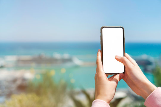Tourist taking a picture with smartphone. Millennial woman traveler making images of seaview with sea liners or ships via cellphone. Hands holding gadget with blurred backdrop view