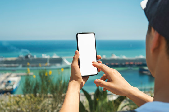 Mockup image, close-up of male hands holding  smartphone and taking photos of seaview with sea liners or ships. Lifestyle travel concept