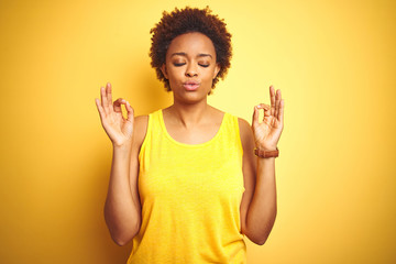 Beauitul african american woman wearing summer t-shirt over isolated yellow background relax and smiling with eyes closed doing meditation gesture with fingers. Yoga concept.