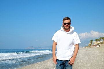 Bearded hipster guy wearing hip white hooded t-shirt at tropical destination. Portrait of young man in black sunglasses smiling over exotic background. Copy space, close up.