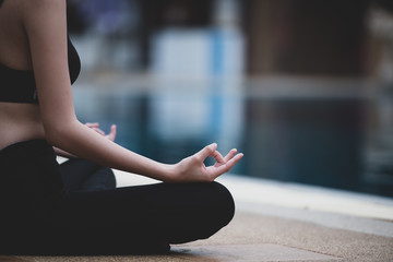 Woman meditating beside swimming pool.