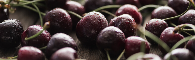 panoramic shot of fresh, sweet, red and ripe cherries covered with water drops on wooden table