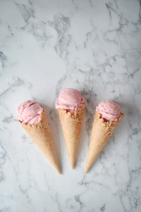 Delicious strawberry ice cream and waffle cone on marble background, top view.