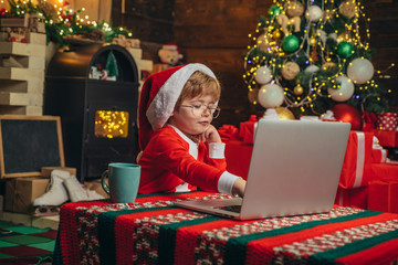 Buy christmas gifts online. Christmas shopping concept. Gifts service. Little genius. Santa little helper. Boy child with laptop near christmas tree. Little boy santa hat and costume having fun