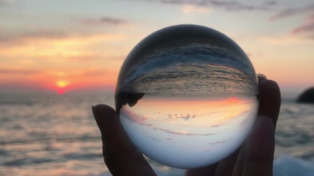 female hand holding in hands crystall ball over beautiful beach sunset