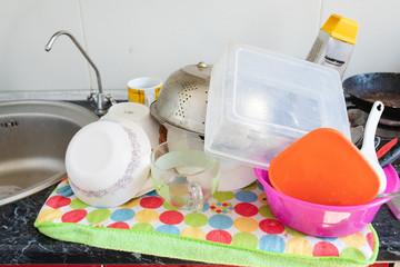 Clean dishes and kitchenware drying on a colorful towel near the kitchen sink. Bowls, containers and cups with utensils.