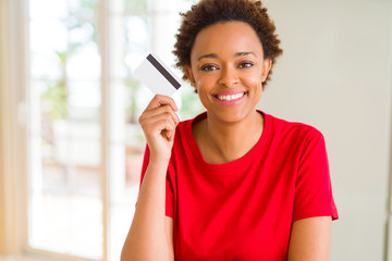 Young african american woman holding credit card with a happy face standing and smiling with a confident smile showing teeth