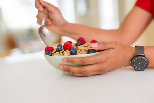 Close up of young woman eating healthy cereals and berries for breakfast