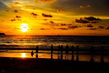 People are playing at the beach and waiting to watch the sunset.