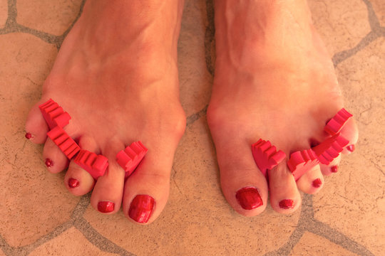 Home made cosmetology. Pedicure of aged woman. Feet with toe divider close up image. Slightly wrinkled skin, valgus, distended veins and other aging changes