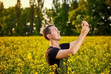 Fototapeta premium A young man farmer or agronomist examines the quality of rapeseed oil on a rape field. Agribusiness concept