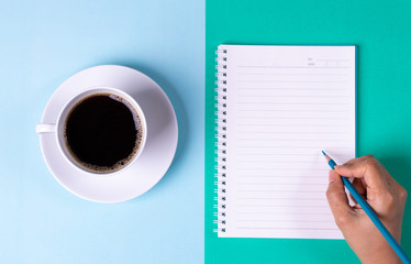 Back to school. Black Coffee and notebook with colored pencil on pastel blue and green table background. Copy space for text.