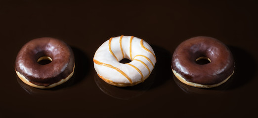 Three glazed donuts on dark  chocolate smooth background. 