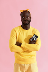 Black man in yellow fashion clothes with photo camera on pink