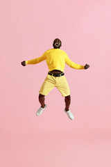 Fototapeta na wymiar Jump. Black man jumping in air and screaming on pink background