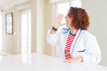 Fototapeta premium Senior doctor woman wearing medical robe at the clinic shouting and screaming loud to side with hand on mouth. Communication concept.