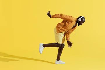 Fototapeta na wymiar Man in headphones listening music, dancing on yellow background