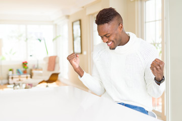 Handsome african american man on white table very happy and excited doing winner gesture with arms raised, smiling and screaming for success. Celebration concept.