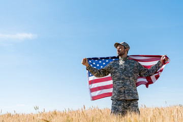 soldier in cap and uniform holding american flag in field