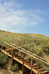 Wooden staircase leading to a hill covered with grass. On the beach. Camping and travelling.